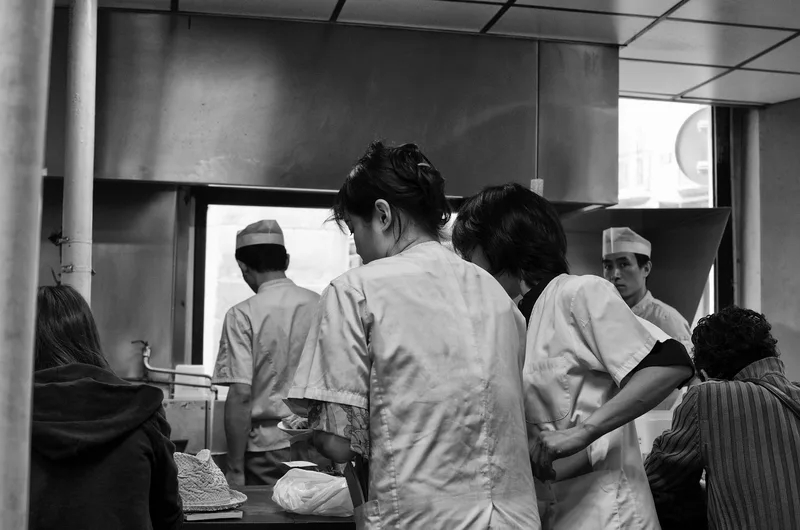 Kitchen staff working behind a counter, black and white