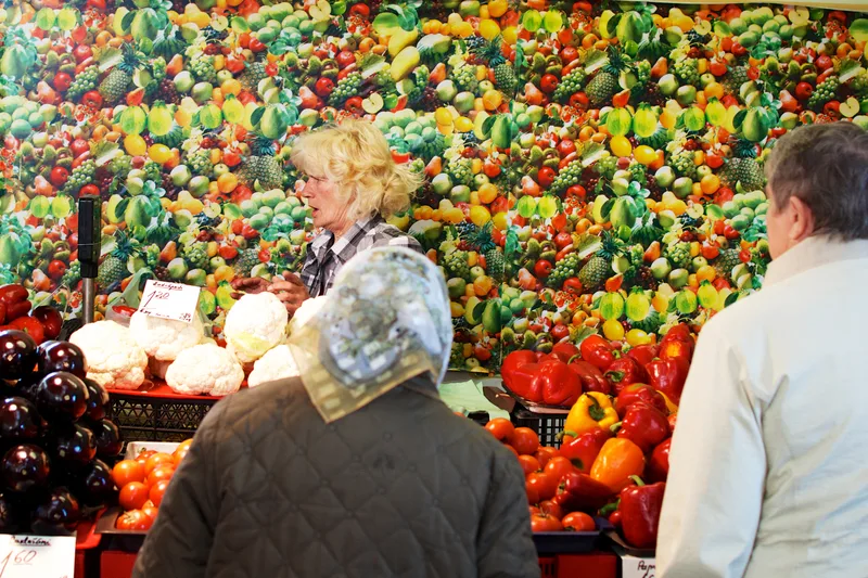 Shoppers at a market stall piled with peppers and tomatoes