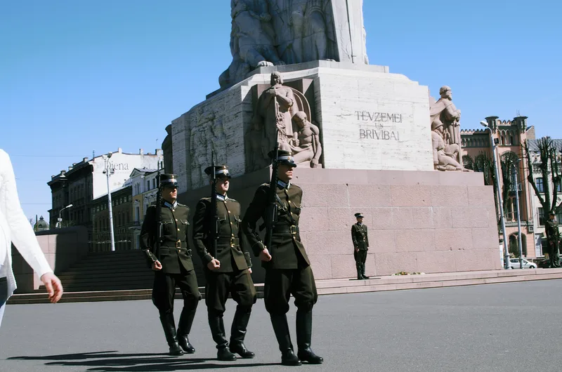 Soldiers marching past a monument under a clear sky