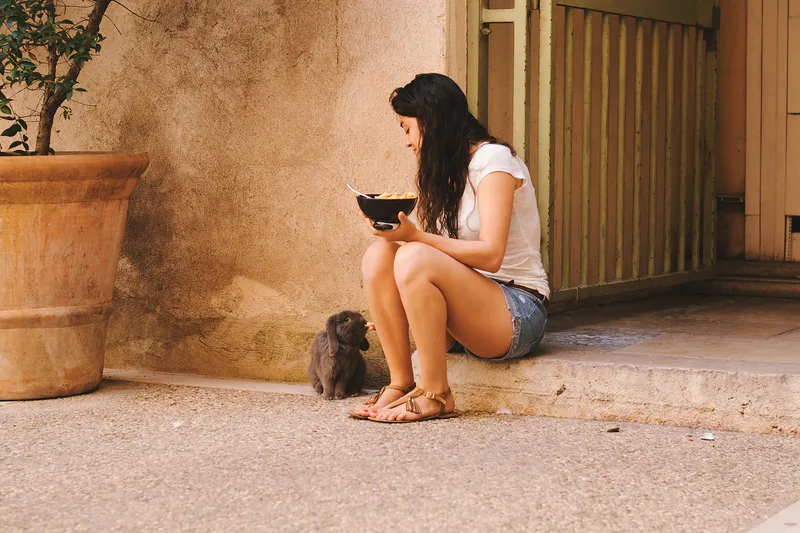 Woman sitting on a step with a bowl, a cat beside her