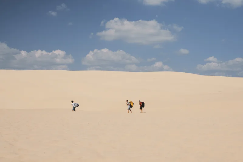 Two small figures walking across a vast pale sand dune