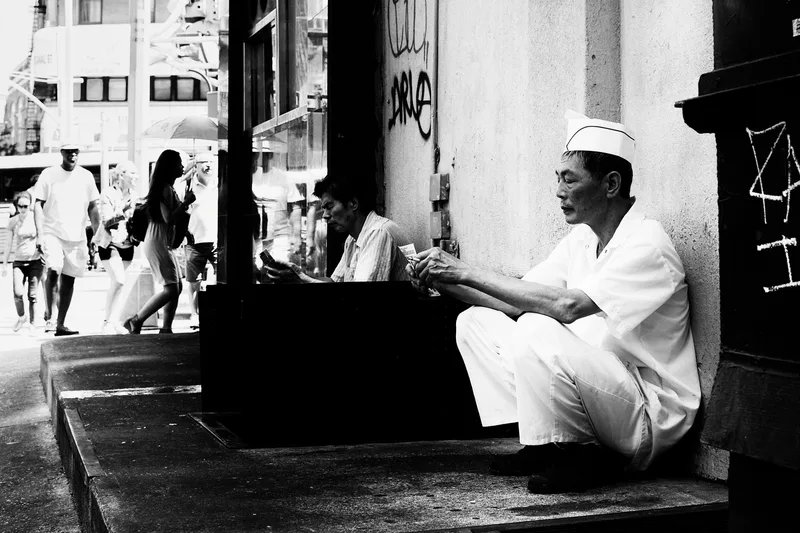 Men seated outside a shop in a narrow street, black and white