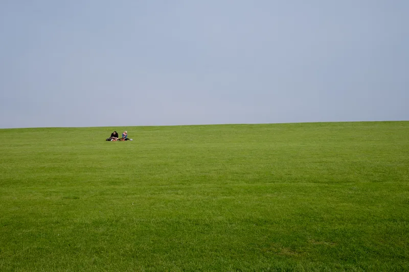 Two people lying on a wide empty green field