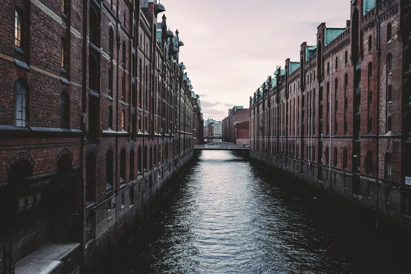 Canal between tall brick warehouses under grey sky
