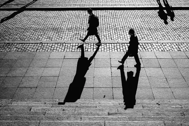 Two figures crossing paving stones, long shadows, black and white