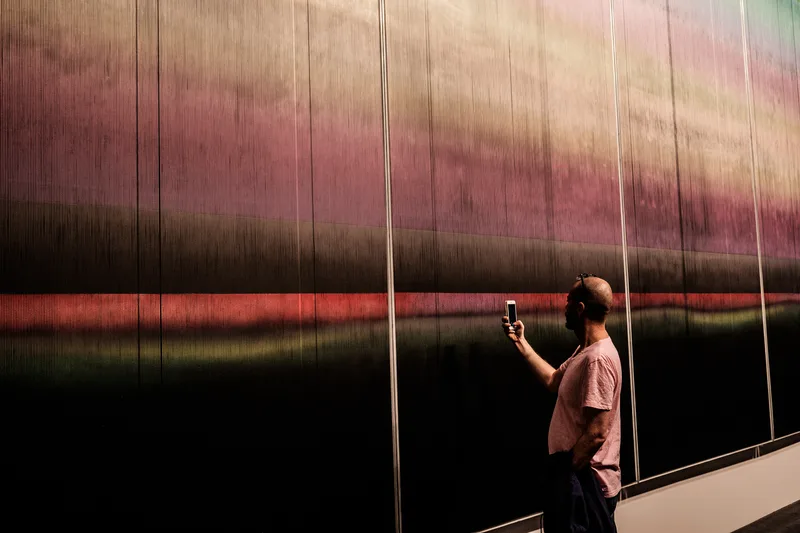 Person photographing a wall of shifting coloured light