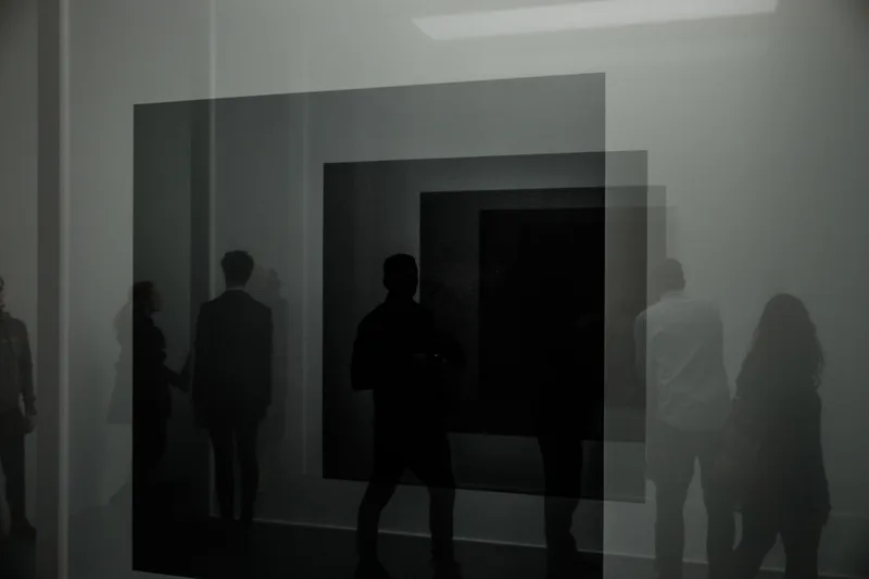 Silhouetted gallery visitors before a large dark artwork