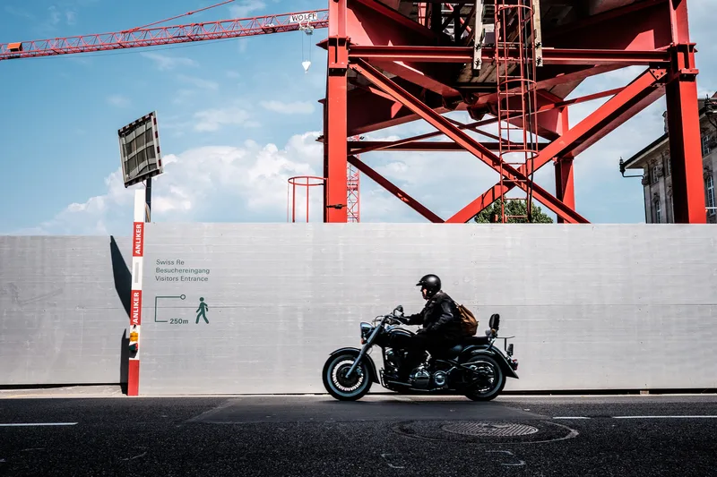 Motorcyclist riding past a red crane and white wall
