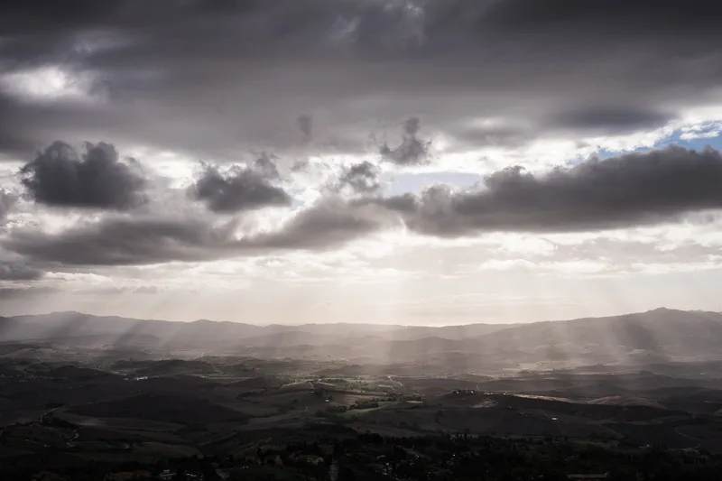 Sunbeams breaking through heavy cloud over a dark valley