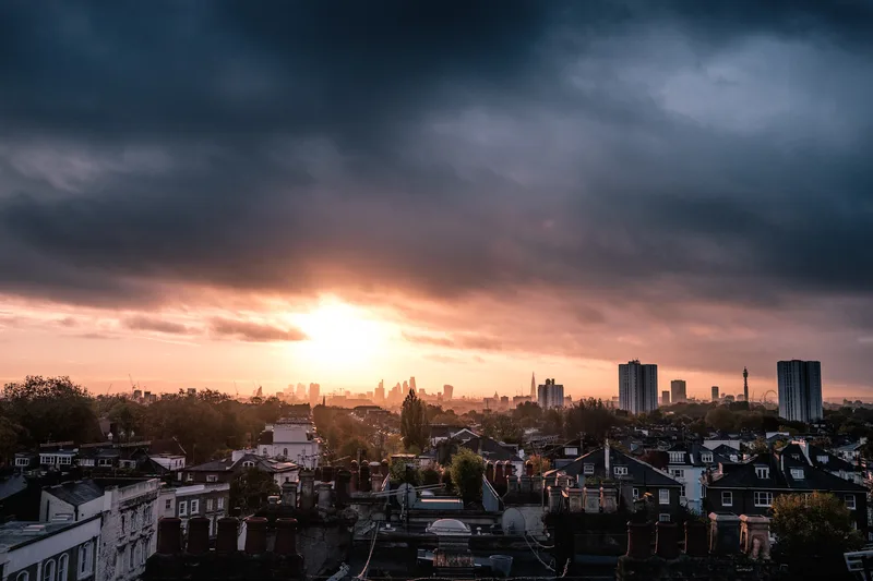Sun setting behind a low city skyline under dark cloud