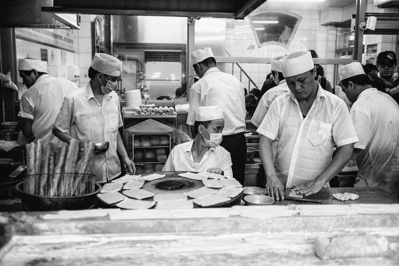 Bakers working over trays in a kitchen, black and white