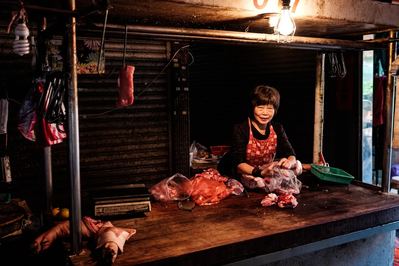 Vendor at a lamplit market stall hung with meat