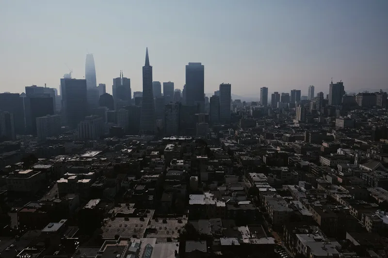 Dense low rooftops below a hazy skyline of distant towers