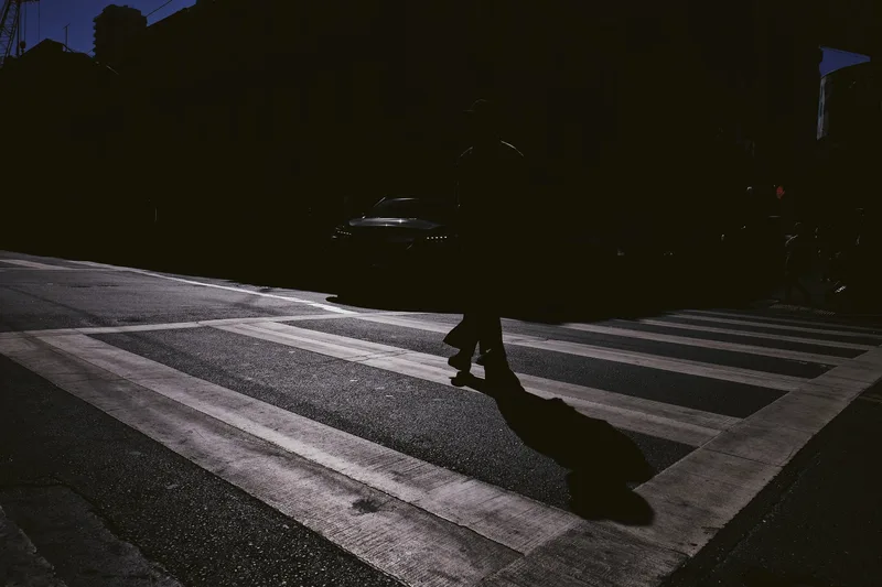 Lone figure crossing a sunlit zebra crossing in deep shade