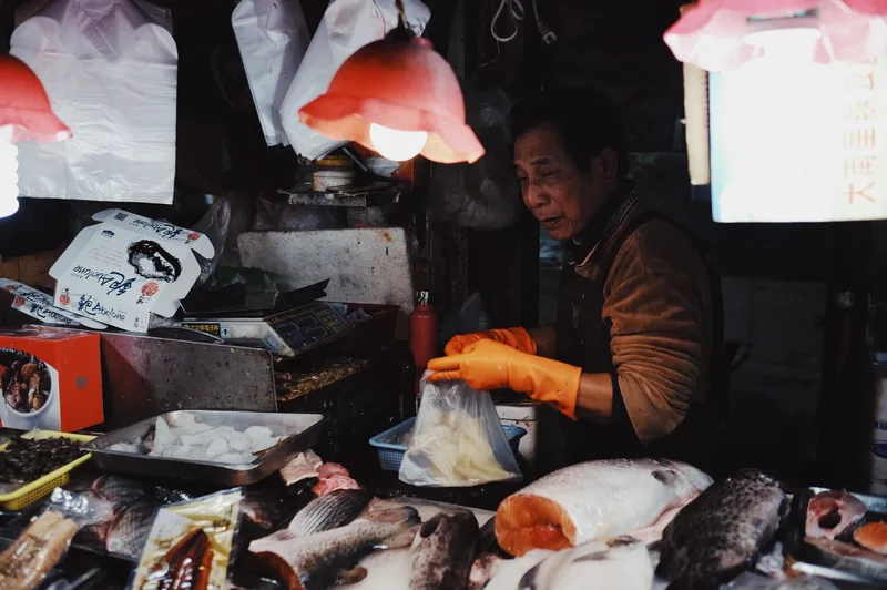 Fishmonger handling fish at a lit market stall