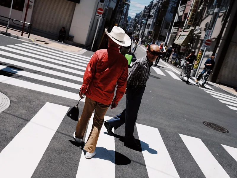 Two men crossing a zebra crossing, one in a red jacket