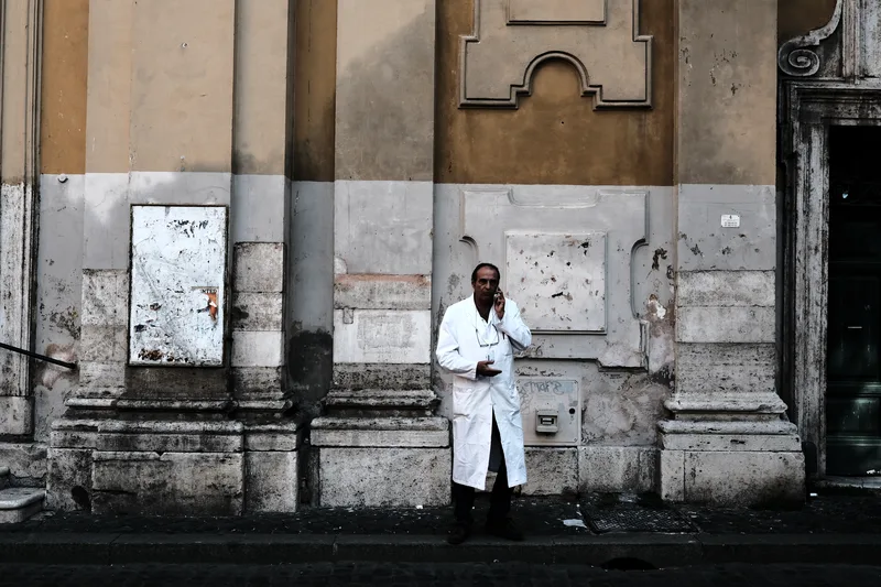 Man in a white coat on a phone beside a weathered wall