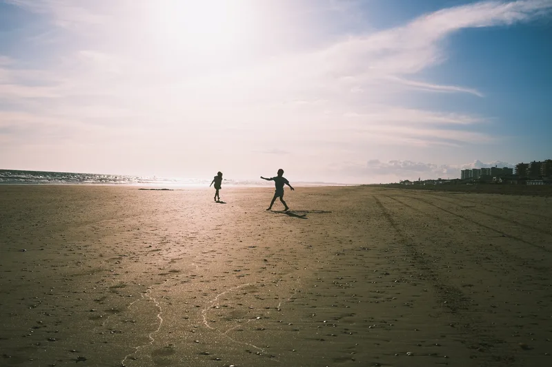 Two figures on a wide empty beach under a bright sky