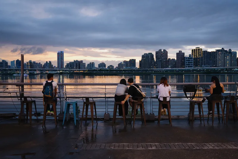 People at a waterfront bar counter facing a city skyline