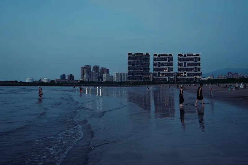 Apartment blocks along a shore at dusk, people wading