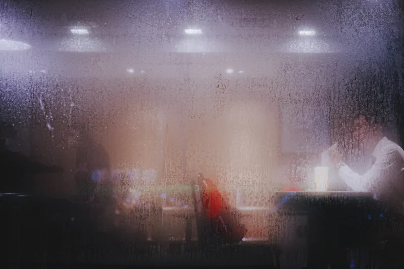 Rain-streaked window over blurred lights and figures