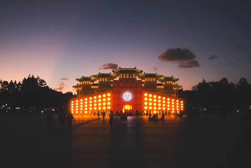 Illuminated ceremonial gate at dusk with a crowd before it