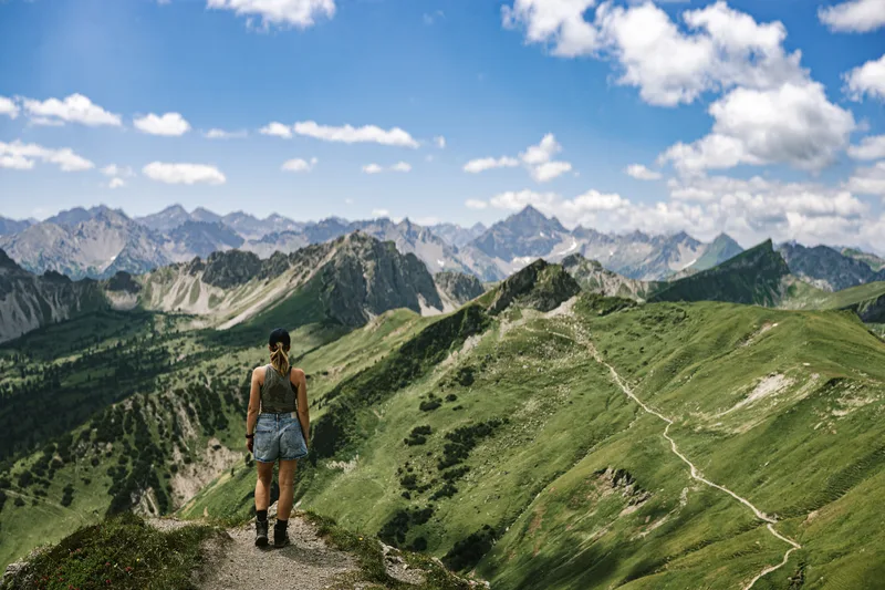 Hiker on a ridge path above green mountain peaks